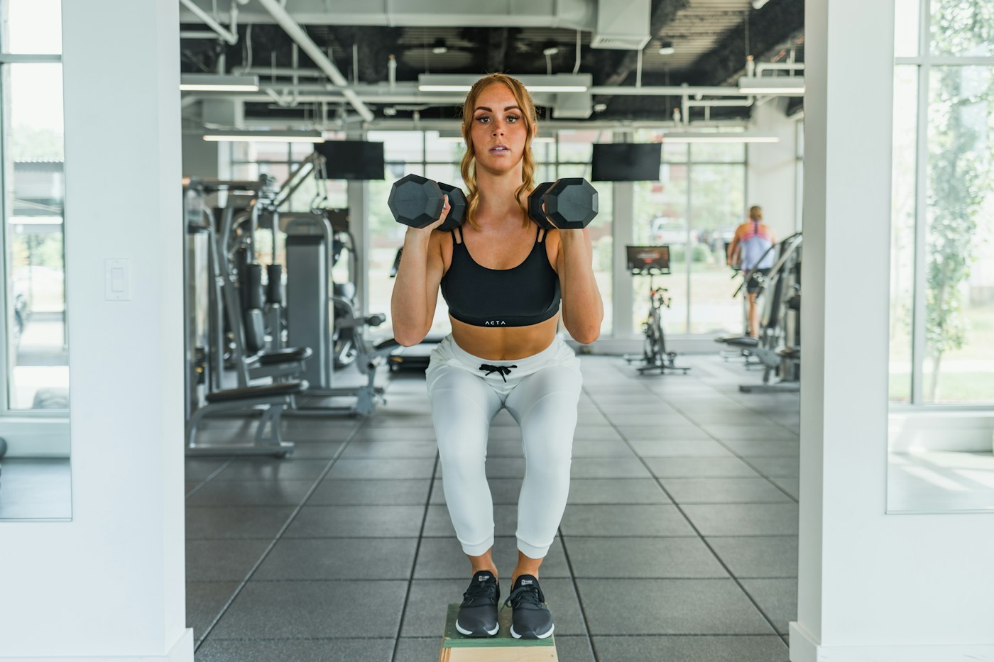 A woman performing a squat while holding two dumbbells